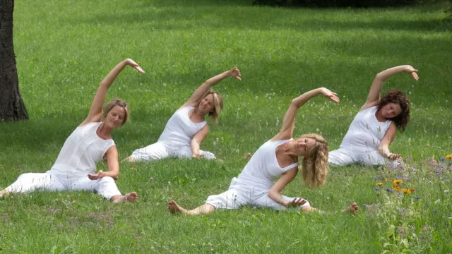 Frauen in weißem Gewand machen im Sitzen eine Yogaübung im Gras