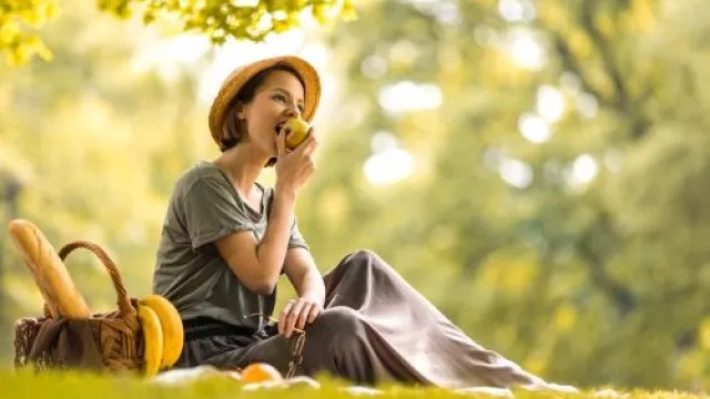 Frau, die auf einer Picknickdecke sitzt und einen Apfel isst
