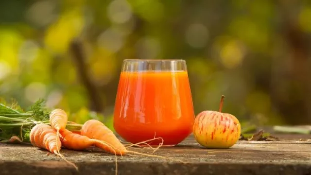Karotten und Apfel, dazwischen steht der gepresst Saft in einem Glas