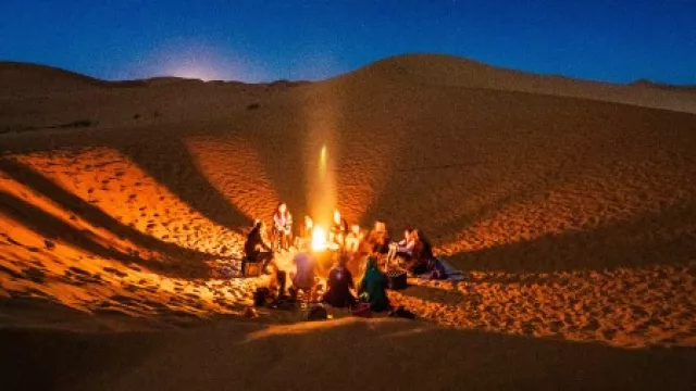 Menschen sitzen in der Wüste in der Nacht rund um ein Lagerfeuer