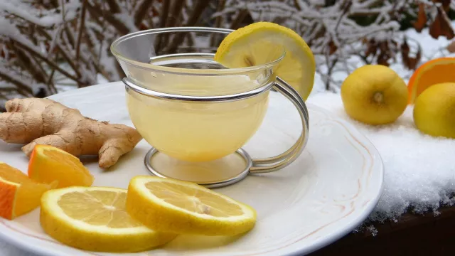 Zitronen Ingwer Wasser in einer durchsichtigen Tasse, mit Zitronenscheiben und Ingwer dekoriert