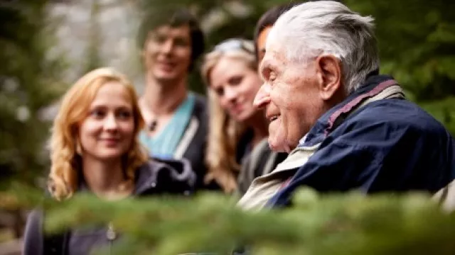 alter Mann sitzt mit einer Gruppe jüngeren Menschen zusammen