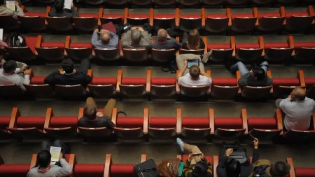 Menschen, die bei einer Konferenz auf roter Kinobestuhlung vereinzelt sitzen