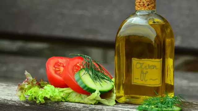 Foto Flasche mit Olivenöl, Tomaten, Gurkenscheiben und Salat daneben