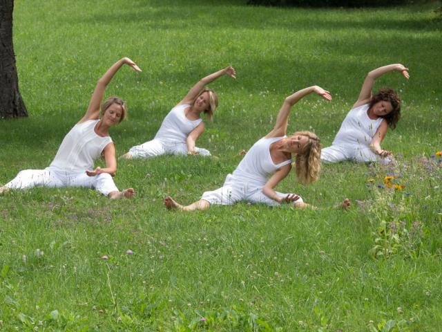 Frauen in weißem Gewand machen im Sitzen eine Yogaübung im Gras